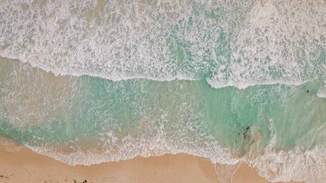 Top down view of turquoise sea waves lapping against golden sand beach in Mexico