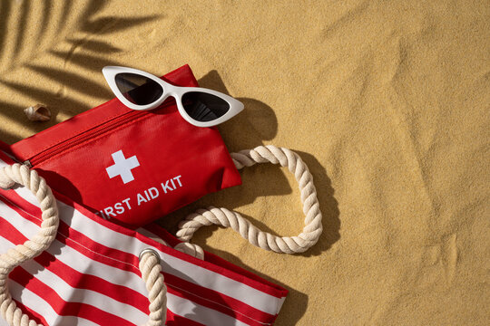 Red first aid kit and striped beach bag on sand highlighting travel health and safety essentials