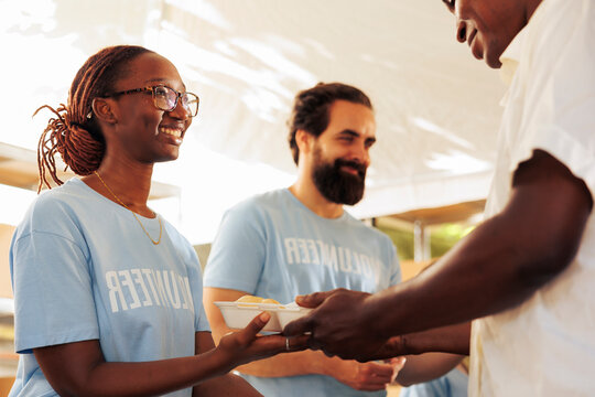 Charitable team provides crucial aid by delivering wholesome meals to individuals who are in need; homeless and least fortunate person served by the african american female volunteer.
