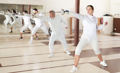 Fototapeta premium Men and women in white uniforms practice fencing techniques with foils in their hands
