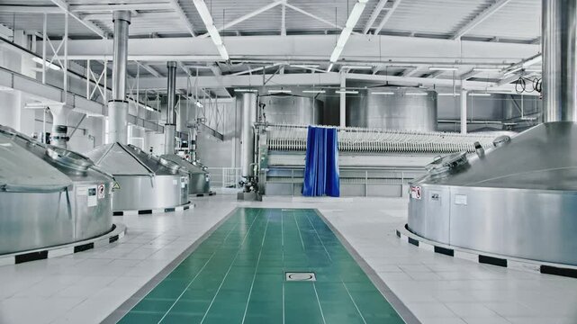 Modern brewery interior with large stainless steel vats for fermenting and brewing beer. Industrial equipment and machinery for alcohol production line inside a clean and sterile factory facility