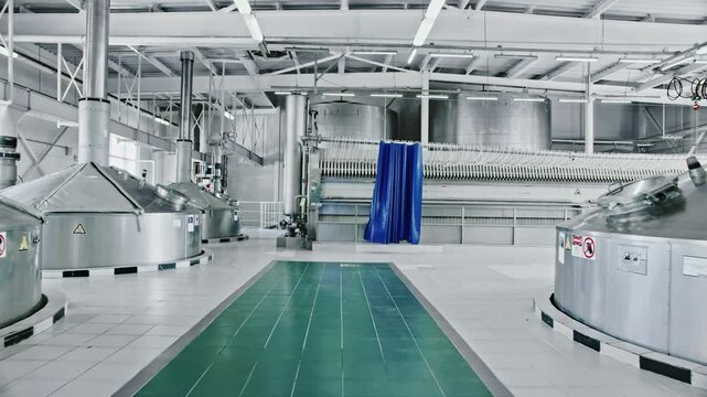 Modern brewery interior with rows of stainless steel fermentation tanks and automated brewing equipment, showcasing a clean industrial production line for beer