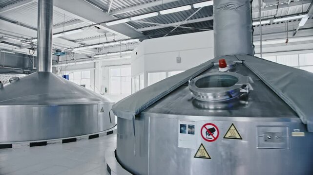 Large stainless steel tanks and vats inside a modern industrial brewery for the production of beer. Automated machinery in a clean and sterile food and beverage manufacturing plant interior