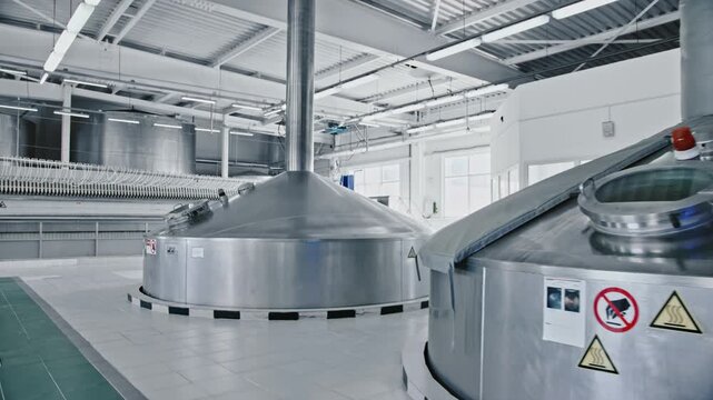 Industrial interior of a modern brewery plant with rows of large steel tanks for beer fermentation and maturation, representing the intricate production process within the beverage facility