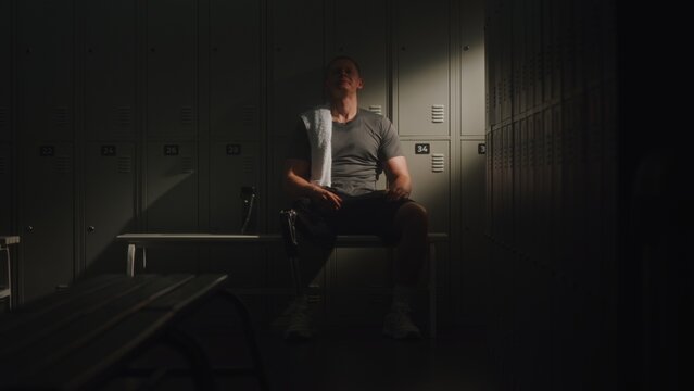 Following Intense Session, Athlete With Limb Loss Retreats to Dressing Room to Restore Energy. Man Sits Down Wearily, Leaning Against Lockers as Beam of Natural Light Fills Space. Inclusive Wellness.