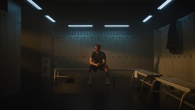 Authentic Fitness Routine. Guy With Short Hair Sits on Bench in Locker Room, Stretching Muscles Under Soft Cinematic Lighting. Active Lifestyle, Body Positivity for People with Limb Loss. Portrait.