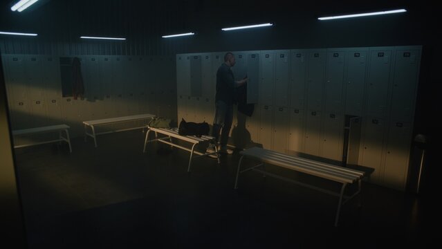 Young Man in Blue Jeans and Vest Enters Modern Locker Room with Noticeable Limp, Opens Grey Locker With Key, and Starts Taking Out Personal Items From Sports Bag. Concept of Inclusion and Diversity.