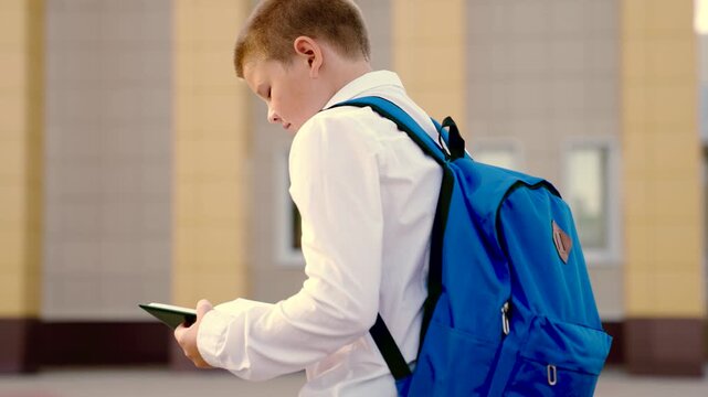 Education, boy child with book and backpack hurries to school. Schoolboy walks with textbook in hand. Pupil child hurries to school for lesson reads book on city street. Children education, learning.
