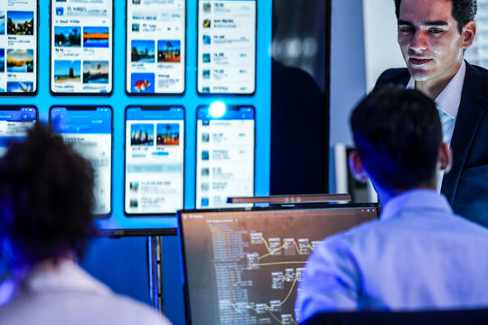 Professional software engineer presenting mobile app UI/UX prototypes and visual node-based logic flow to a development team in a high-tech office.