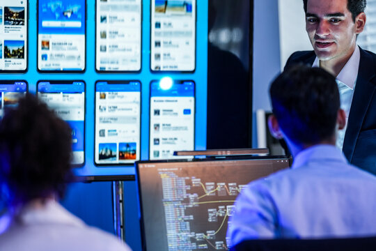 Professional software engineer presenting mobile app UI/UX prototypes and visual node-based logic flow to a development team in a high-tech office.