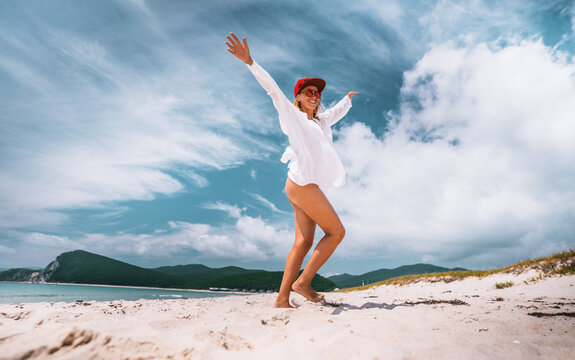 Happy woman enjoying summer day on beach with open arms under blue sky. Freedom, balance and positive lifestyle concept with travel and nature