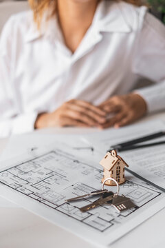 Woman presents keyring and house model over architectural plans during mortgage consultation. Concept of financial responsibility, property acquisition and long term investment.