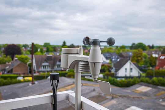 Home weather station anemometer on balcony railing measuring wind speed and direction with suburban background