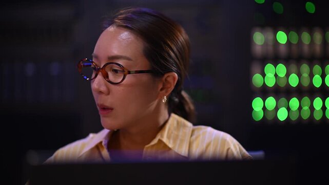 Female it support engineer analyzing data and solving problems on a laptop in a modern server room at night