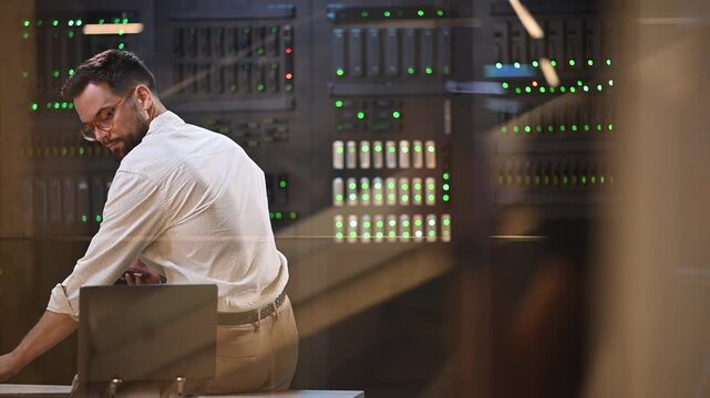 It administrator managing server rack hardware in a data center using a smartphone and laptop for network diagnostics