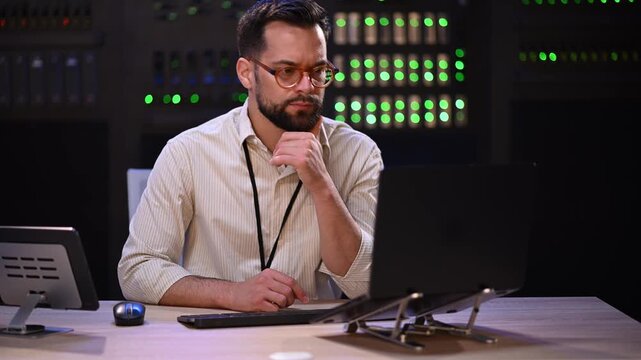 It support specialist working on a laptop computer in a network server room at a data center and thinking about a problem