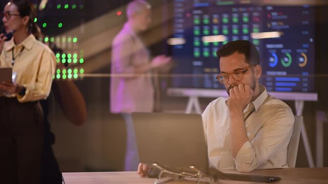 Stressed it specialist working on laptop analyzing data in a server room getting worried about a problem