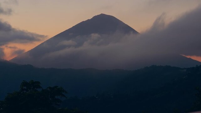 Close View of Mount Abang Covered by Flowing Clouds at Sunrise, Volcanic Peak Emerges Above Forested Highlands In Peaceful Morning Atmosphere