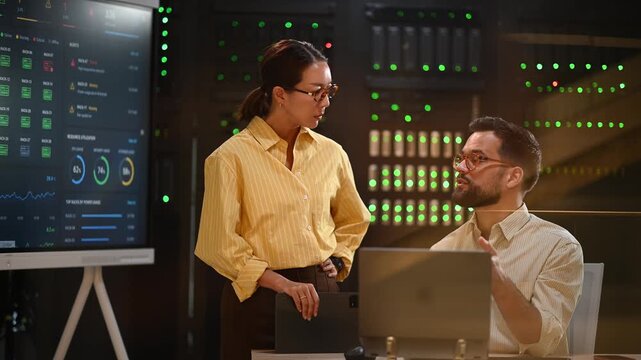 It professionals collaborating in data center, managing servers on laptop with futuristic digital analytics on screen