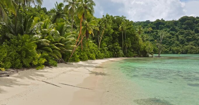 Lush green jungle meets a white sand tropical beach with clear turquoise ocean water gently lapping shore under a partly cloudy sky at Teague, Torres Islands Vanuatu. Summer vacation tropical paradise