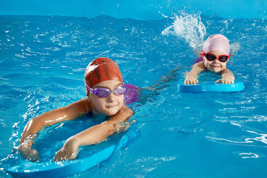 Two little girls learning to swim in indoor pool with pool board