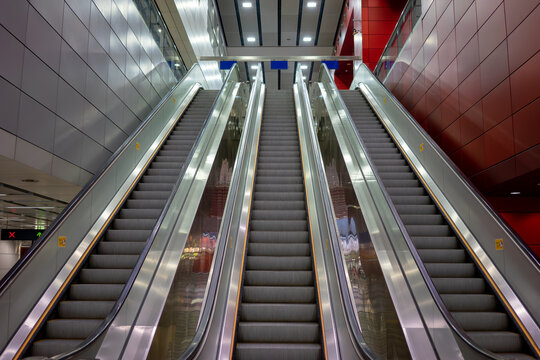 Symmetrical low-angle view of multiple modern escalators in a public transit station or shopping mall interior.