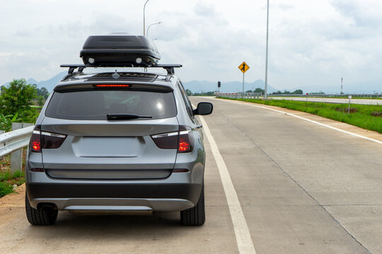 SUV Car with Roof Cargo Box Parked on Shoulder of Empty Highway