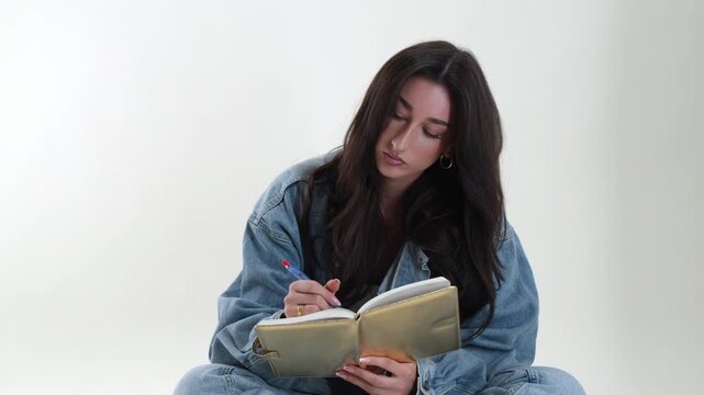 Creative writing and self reflection concept with a young woman writing in a notebook using a pen. This studio shot captures her thoughtful concentration, themes of education, personal development, an