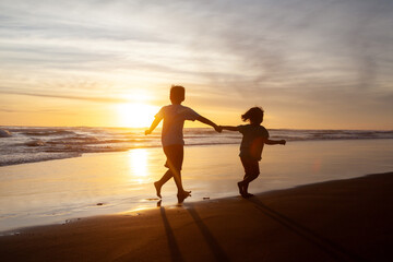 Fototapeta premium Happy Children Silhouette Running and Holding Hands on the Beach at Sunset
