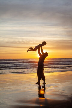 Father lifting young child in the air on beach at sunset, silhouette