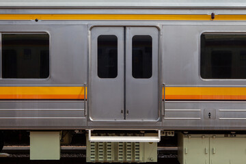 Side View of a Stainless Steel Passenger Train Car with Closed Sliding Doors, Windows, and Yellow Stripe Accents © Creativa Images