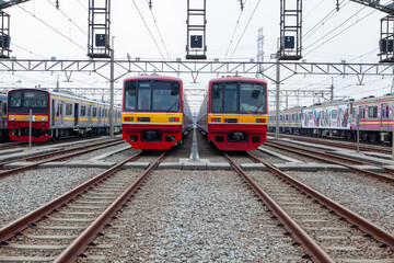 Obraz premium Symmetrical Low-Angle Shot of Red and Yellow Commuter Trains Parked at a Rail Yard Depot on Multiple Tracks