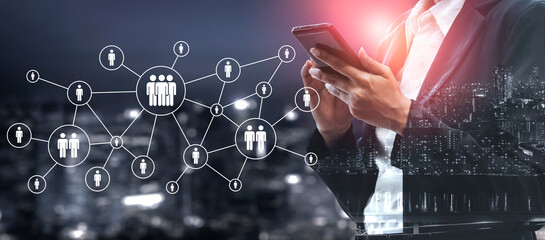 A business professional stands in an urban environment at night, using a smartphone while surrounded by abstract icons representing digital connections and networking. Ledger © InfiniteFlow