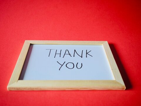 A close-up, low-angle shot of a minimalist wooden frame whiteboard with the handwritten text "Thank You" centered on a solid red background.