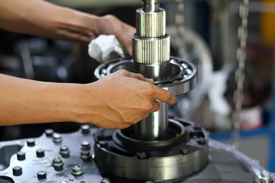 Close-up of mechanic hands carefully installing a large metal ball bearing onto a steel transmission shaft during mechanical repair.