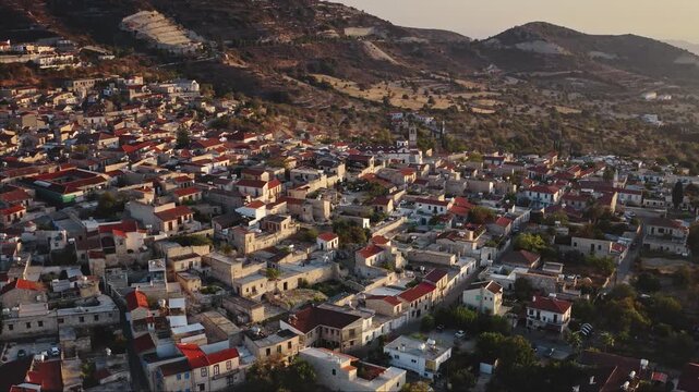 Pano Lefkara village in Cyprus with clustered red tiled and stone houses buildings on sunlit hills, historic Mediterranean townscape at warm summer sunset. Travel destination. Aerial view drone flight