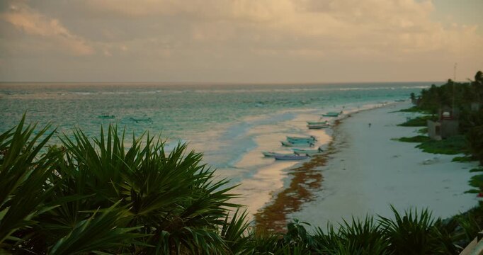 Caribbean beach with boats palm leaves and soft waves glows at sunset in Tulum Mexico