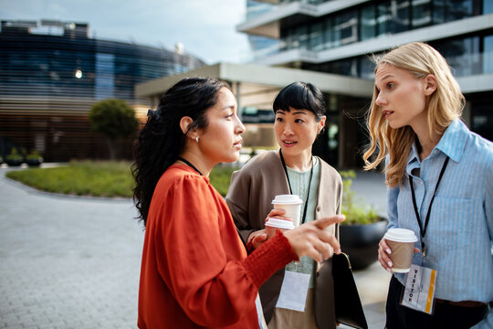 Three businesswomen networking with coffee outside modern office building