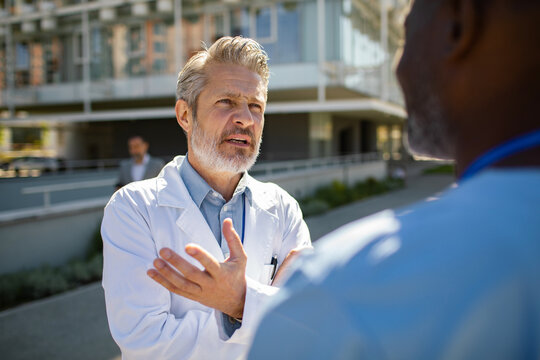 Senior doctor discussing care with colleague outside hospital