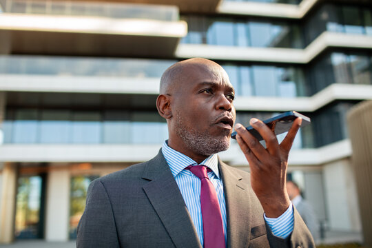 Business executive using smartphone voice assistant outside modern office