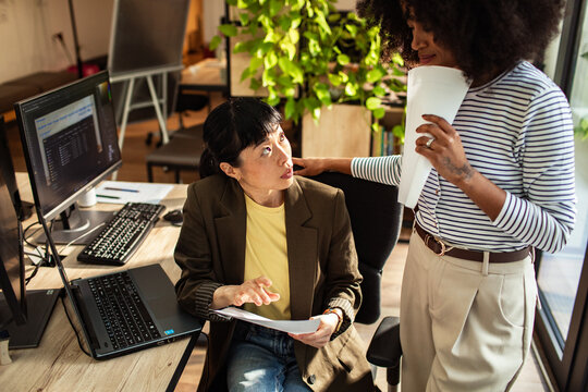 Two coworkers discussing project at desk in modern office