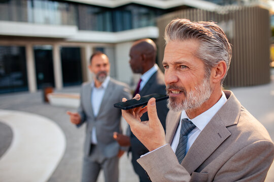 Mature businessman using voice assistant outside office