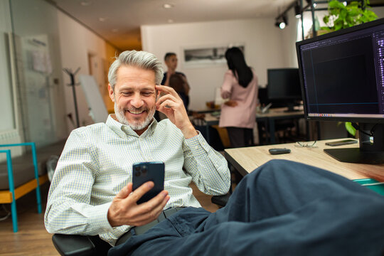 Smiling mature man using smartphone at office desk