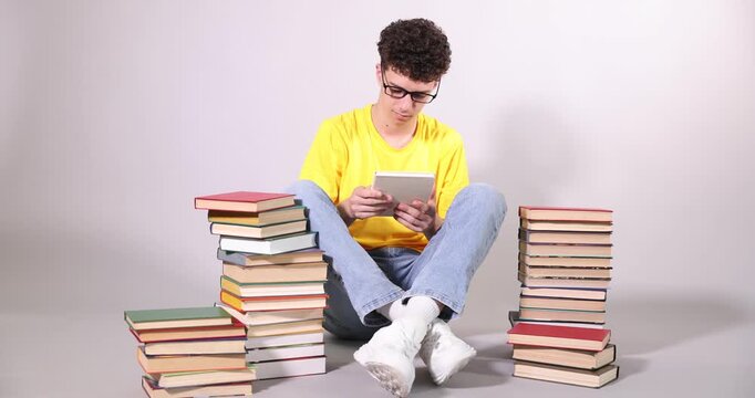 Teenage boy reading and stacks of books on light grey background