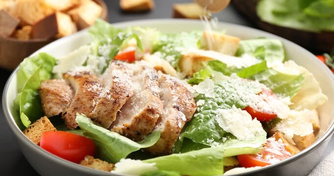 Adding cheese to Caesar salad at table, closeup
