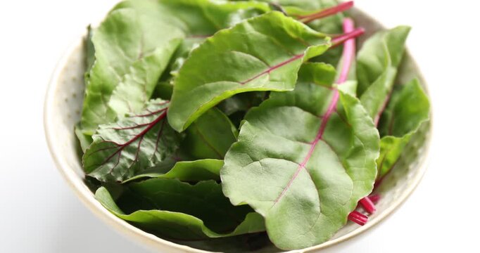 Spraying fresh beetroot leaves with water at white table, closeup