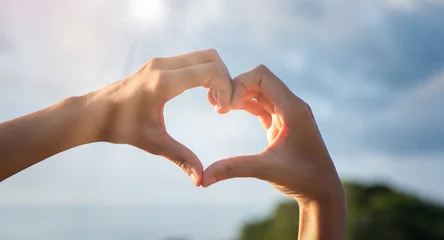 Girl hands in shape of love heart on blue sky with cloud. © nuttawutnuy