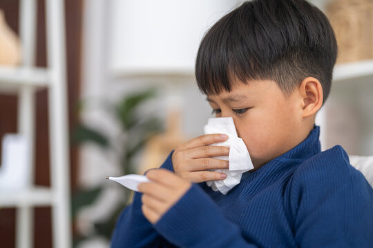 Sick asian boy child wiping runny nose with tissue and checking a digital thermometer for high fever temperature, Concept of flu symptoms, child health care, rsv, influenza and bronchitis illness