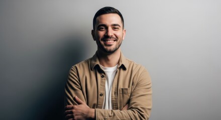 Obraz premium Portrait of a Confident and Happy Young Man Smiling with Arms Crossed Against a Neutral Grey Background