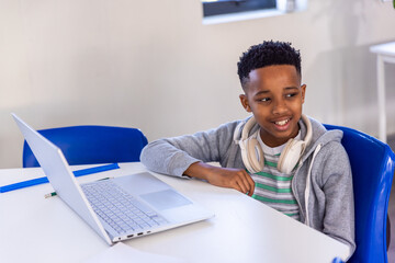 Obraz premium African American boy child sitting in class with gray hoodie, white headphones, silver laptop